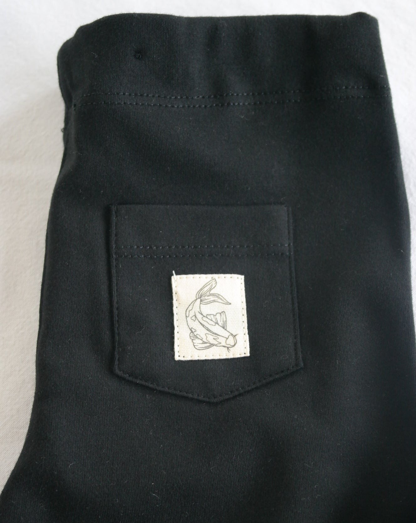 Leggings made from 100% GOTS certified organic cotton in black, with Koi fish cotton badge at back pocket. Elastic adjustable waist, foldable cuffs at the bottom of the legs.