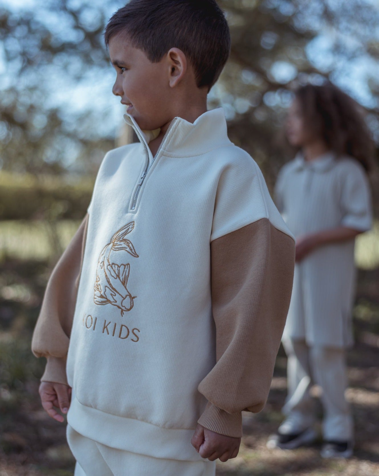 Offwhite sweatshirt with light brown Koi fish logo embroidery at front. With zipper neckline and brown contrast sleeves, foldable cuffs with an oversized fit.