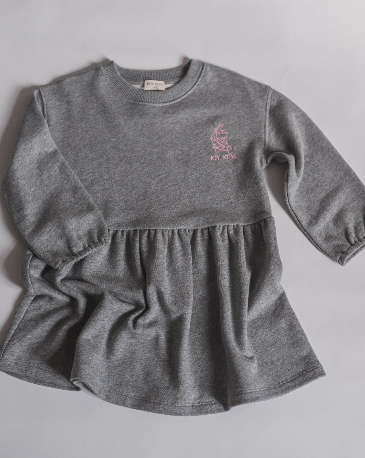 Long sleeved sweatshirt dress in grey mélange jersey fabric and the Koi Kids logo at chest. Cut for an oversized fit with slightly ballon shaped sleeves, a high waist and a flared skirt.