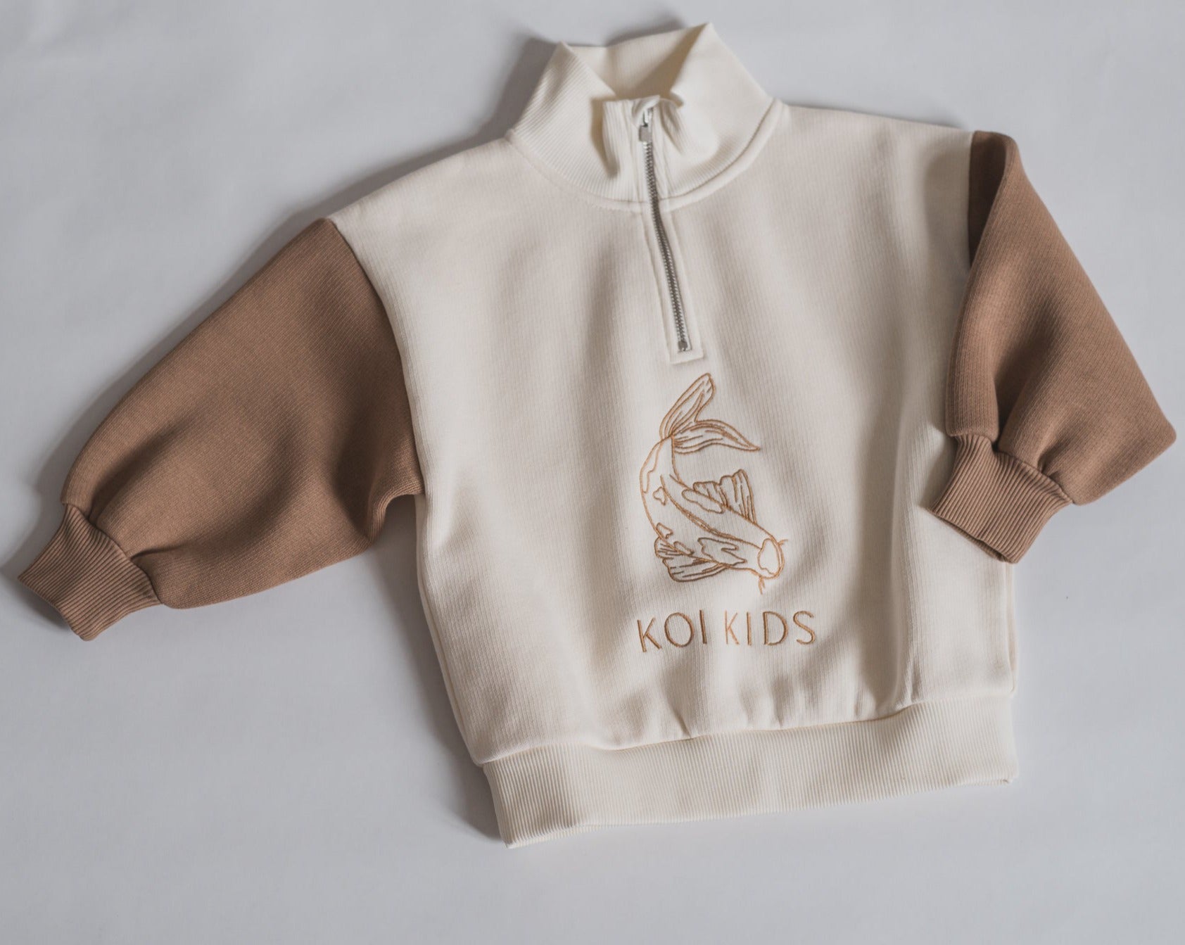Offwhite sweatshirt with light brown Koi fish logo embroidery at front. With zipper neckline and brown contrast sleeves, foldable cuffs with an oversized fit.