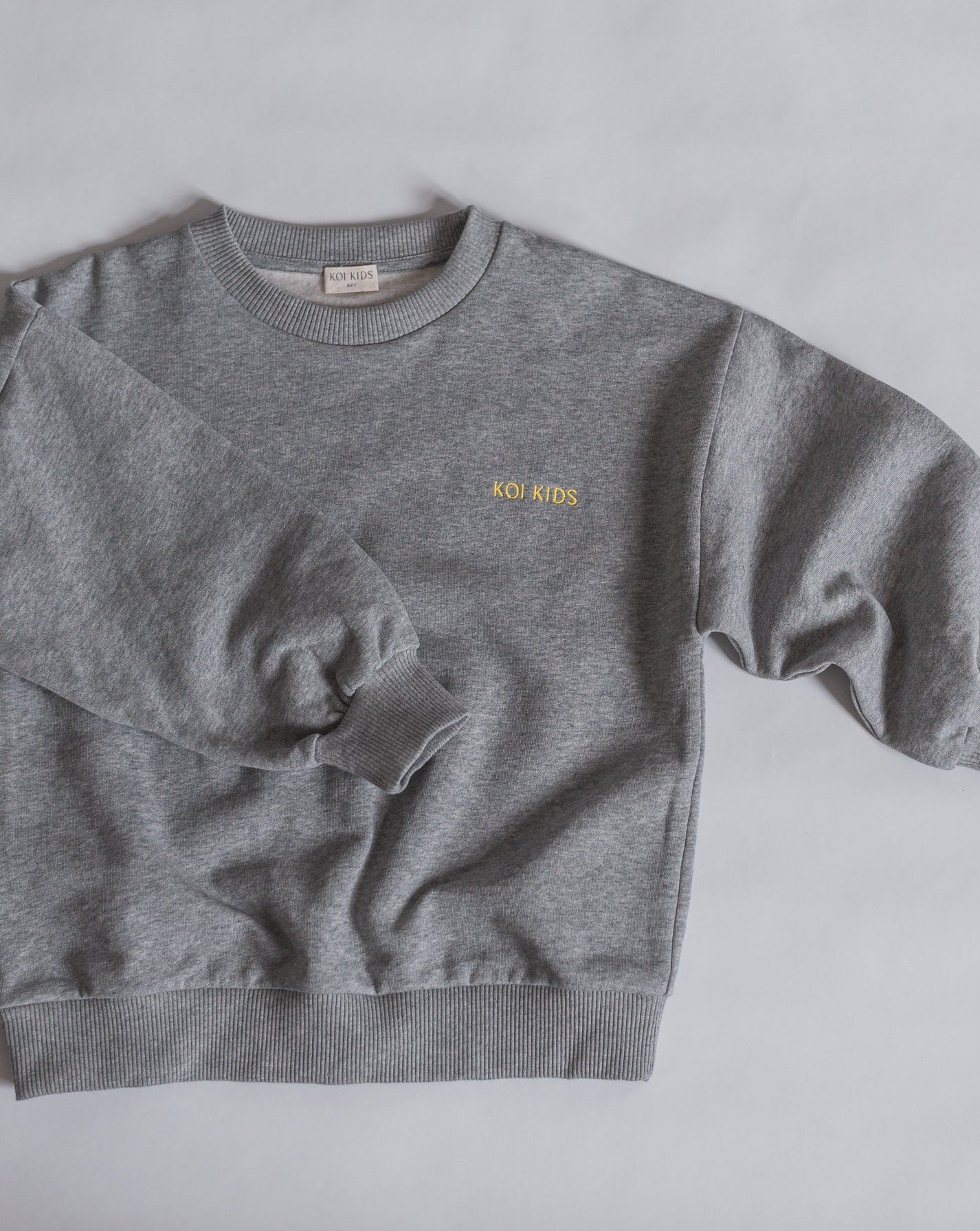 Grey mélange sweatshirt with yellow logo embroidery, dropped shoulders and foldable cuffs with an oversized fit.