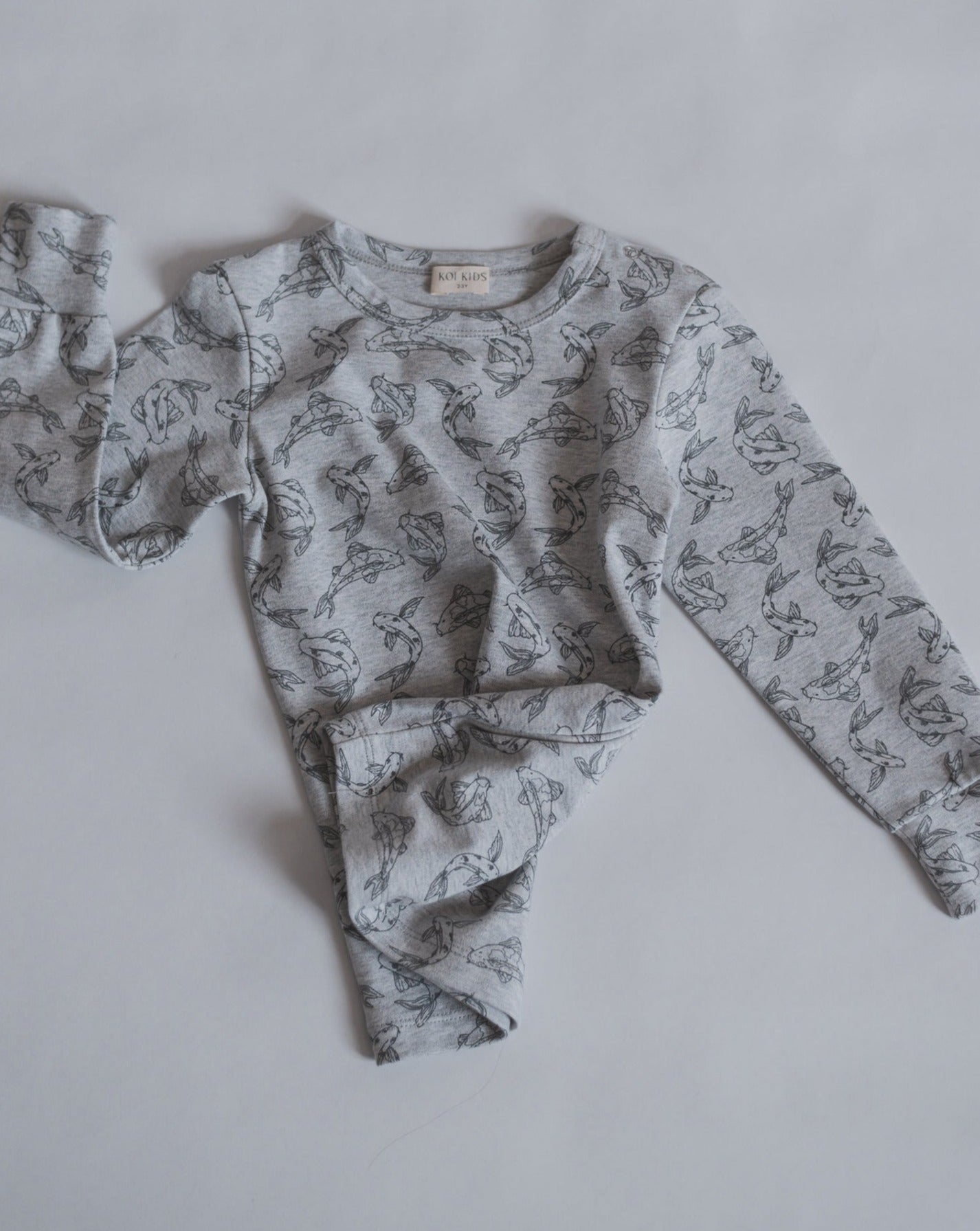 Allover printed long sleeve with our signature Koi fish print in grey mélange. With round neck, press buttons at shoulder. Extra length added to the body for a loose and relaxed look.