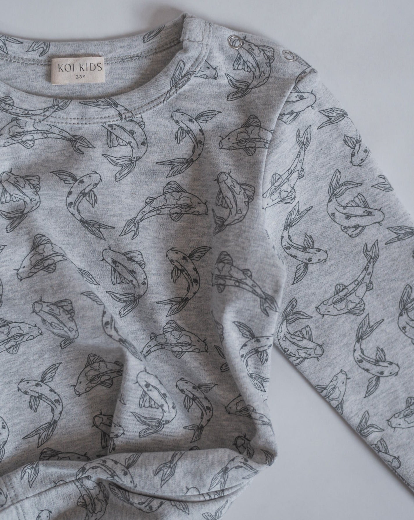 Allover printed long sleeve with our signature Koi fish print in grey mélange. With round neck, press buttons at shoulder. Extra length added to the body for a loose and relaxed look.