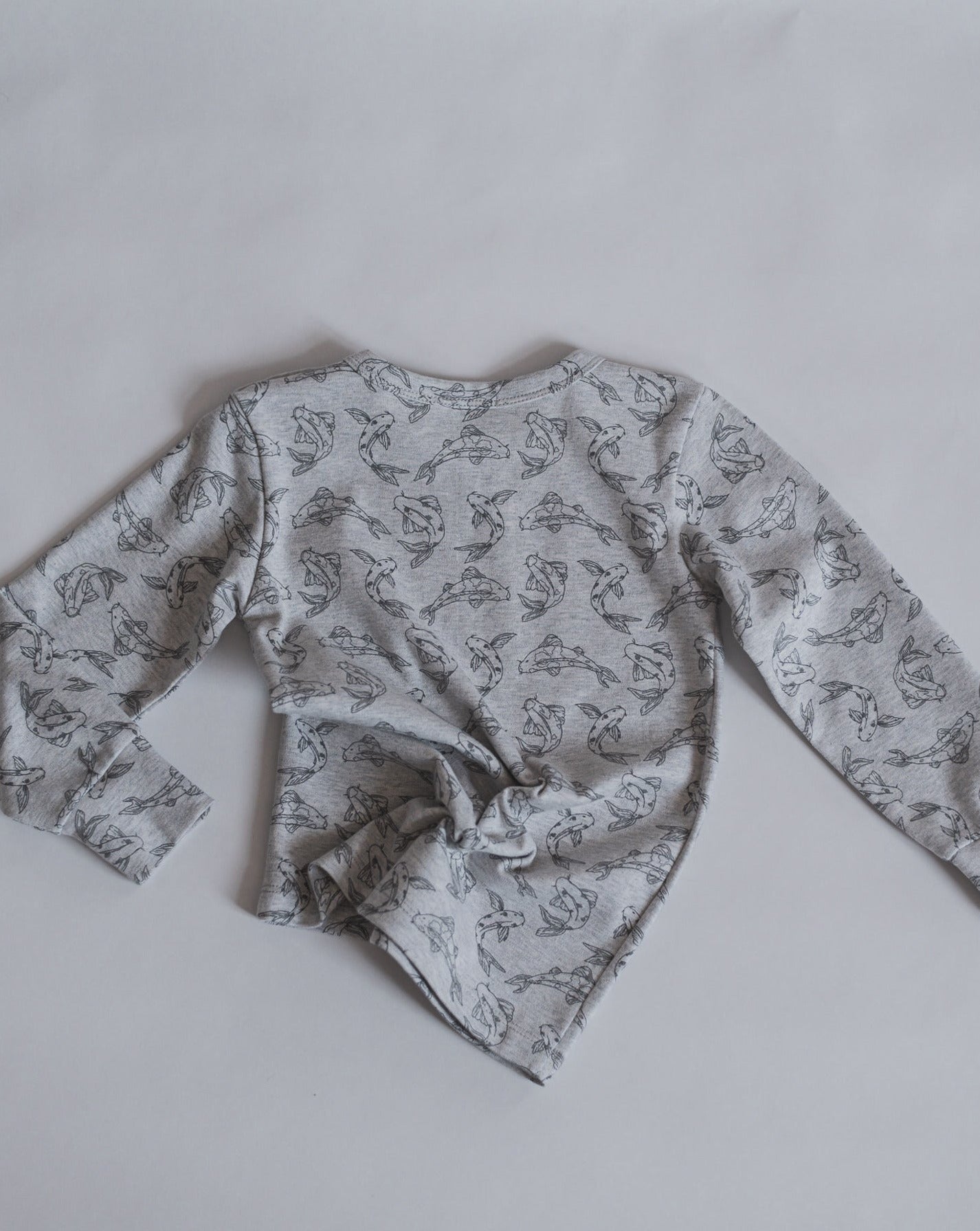 Allover printed long sleeve with our signature Koi fish print in grey mélange. With round neck, press buttons at shoulder. Extra length added to the body for a loose and relaxed look.