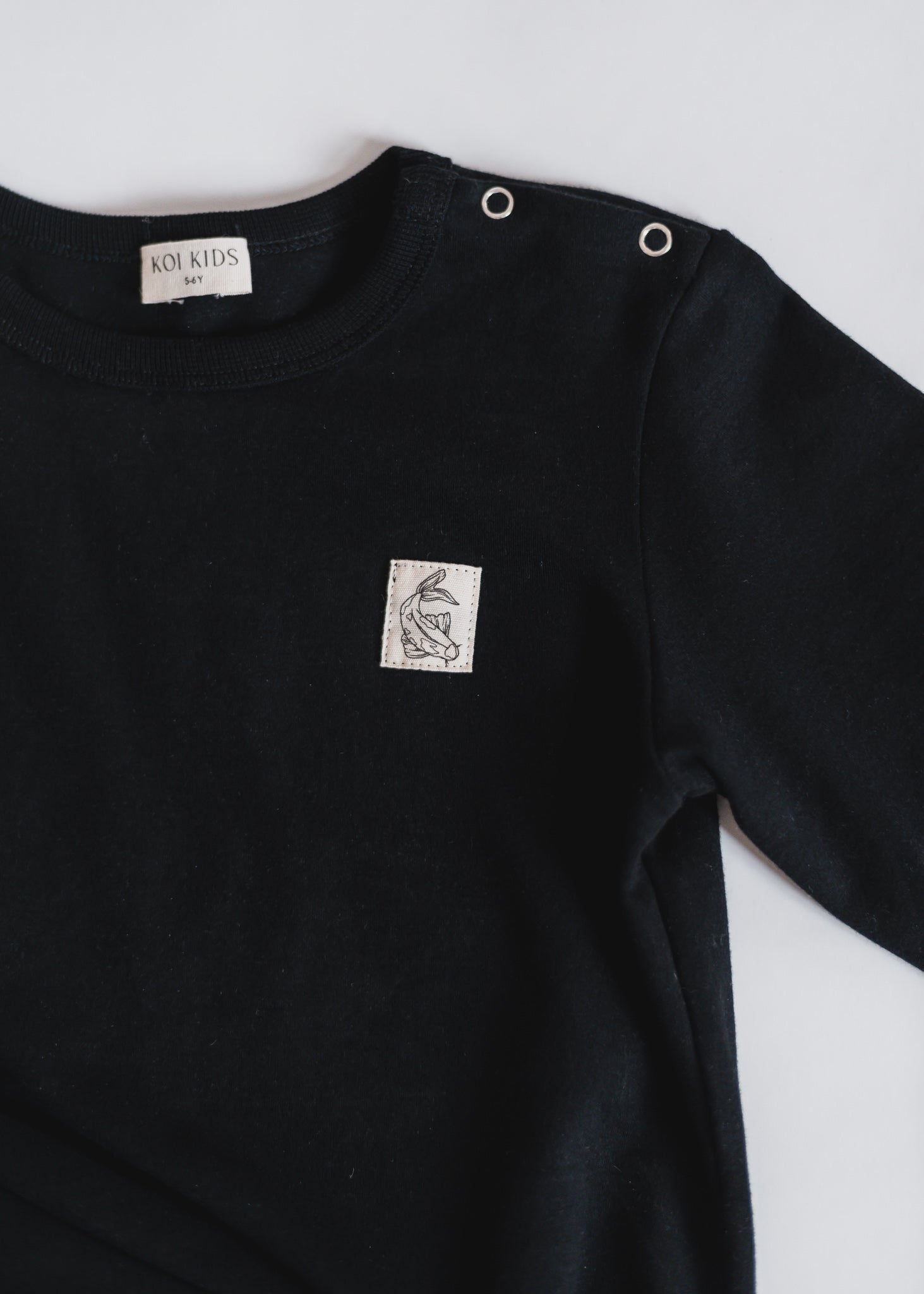 Black long sleeve with our signature Koi fish cotton badge at chest. With round neck, press buttons at shoulder. Extra length added to the body for a loose and relaxed look.